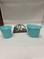 Front view of two turquoise Robin Blue Tupperware containers next to a metal napkin holder with floral decoration.