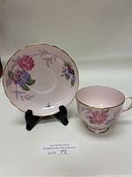 Front view of pink floral teacup and scalloped edge saucer with gold trim on display stands