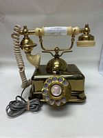 Front view of the brass and plastic Victorian style rotary dial telephone with coiled handset cord.