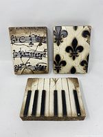 Front view of three Sid Dickens decorative wall tiles: piano keys, musical notes, and fleur-de-lis.