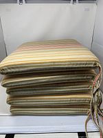 Stack of 5 outdoor chair pads with beige, yellow, and green stripes viewed from the side showing thickness and ties.