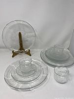 Full view of some clear glass plates, cups, and saucers showing the floral textured pattern on the edges.