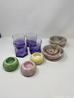 Overview of the lot showing 4 purple old fashioned glasses, 2 hand-painted Hilborn pottery bowls, and 3 round colorful stone tealight holders in green, yellow, and pink.