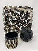 Top view of three decor pieces showing a metallic leaf wall sculpture, black geometric sculpture, and small striped vase.