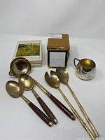 Photo showing four Thai brass serving utensils including ladles with wooden handles, serving spoons with long brass handles, four stacked Pottery Barn brass picture frames in box, and silverplated creamer.