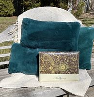 Three teal faux fur cushions placed on woven beige throw with new packaged Mahogany kingsize duvet cover in front.