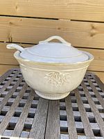 Front view of the Pottery Barn soup tureen with lid and ladle on wooden surface.