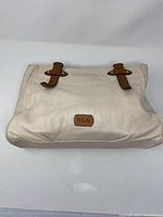 Front view of off-white Ralph Lauren purse showing brown leather handles and RLL logo plaque with clear ink stain on surface.