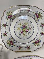 Close-up of Petit Point square floral plate with multicolor floral design and textured pattern, gold rim trim