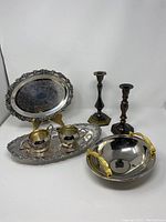 Full lot showing silver plated oval dishes, cream and sugar set, metal bowl with gold tone handles, and two metal candlesticks.