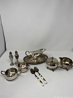 Lot items arranged against white backdrop showing overall set including spoons, cream and sugar containers, salt and pepper shakers, gravy boat, and undertray