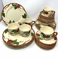 Vintage Franciscan Apple pattern plates, bowls, and cups arranged showing the hand-painted apple and leaf designs on the fronts.