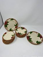 Seven saucers, six bread and butter plates, and three lunch plates with the red apple and green leaf pattern, arranged in three groups on a white background.