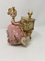 Full view of the porcelain figurine of a young girl playing a piano music box, showing dress, piano details, and position of figurine.