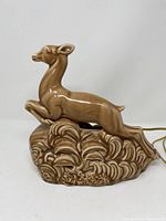 Side view of brown ceramic lamp shaped as a leaping deer on decorative base