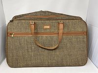 Full front view of rectangular tweed overnight bag with leather handles and front zippered pocket.