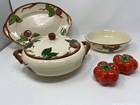 Full view of five items including the covered vegetable dish, oval platter, open bowl, and two tomato-shaped salt and pepper shakers arranged on a surface.
