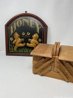 Photo showing both the wooden 'HONEY' wall sign with dancing bears, and a wooden accordion style sewing kit box.
