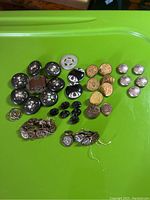 View of assortment of antique buttons laid out on green surface showing different styles and materials including black wood with shell, brass, silver, and glass buttons