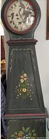 Front view of forest green Mora grandfather clock decorated with painted flowers and a glass door over the clock face showing faded Roman numerals.