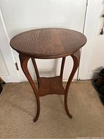 Front view of antique round tiger oak lamp table showing curved legs and round top.