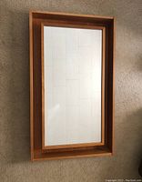 Front view of rectangular wood-framed mirror lying face up on floor, showing mirror surface and frame