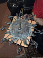 Top view of metal sun face with green patina showing detailed facial features and sun rays.