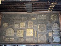 Photo of brass printing plates arranged in multiple rows on a wooden tray with labels showing sizes 25, 20, 30.