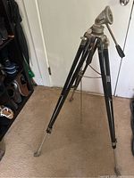 Full view of the tripod showing its three black metal legs, adjustable height and handle for adjusting the head.