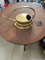 Full side view of vintage solid brass watering vessel with handle and spout on wooden table.