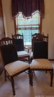 Four wood-framed chairs with upholstered seats and backs. Three side chairs and one armchair with wood armrests. Positioned near a window and wooden door.