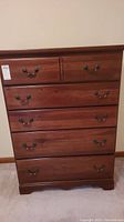 Front view of Vaughn Bassett wooden tall boy chest with five drawers and metal handles, showing scratches and wear.
