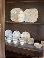 China set displayed in a cabinet showing cups, saucers, plates, and teapot with lid.