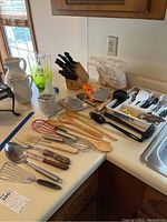 Overview of kitchen utensils on counter including knife block with knives, various spoons, graters, hand mixer, and pitchers