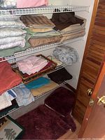 Closet shelves filled with folded bed linens, towels, and bath mats. Items are organized by type and color.