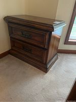 Pair of dark wood night stands with carved details and two drawers each, shown in corner position on carpeted floor.