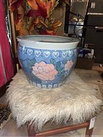 Full front view of ceramic planter on a chair with fur covering, showing blue background and pink roses with leaf details.
