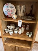 Shelf containing decorative ceramic plates, bird figurine, ceramic tea set and sake set, and stone bookends.