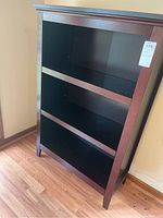 Front view of the dark wooden bookshelf showing three shelves with some scratches.