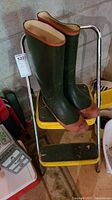 View of the folding step stool with the green rubber boots placed on the top step, showing the condition and size relation.