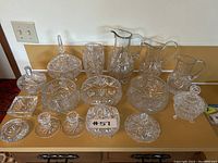 Full set of sixteen clear crystal pieces arranged on counter under lighting showing detailed pinwheel cut pattern.