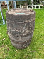 Large weathered wooden barrel standing upright on grass with metal bands, showing outdoor wear and tear