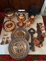 Entire collection arranged on a white cloth showcasing copper items, decorative plates, cast iron stove, and tools