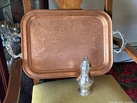 Small silver shaker in front of copper tray on a green chair