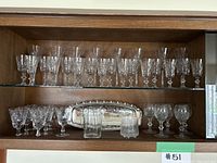 Shelf display of various crystal stemware glasses and a silver plated tray arranged on two glass shelves.
