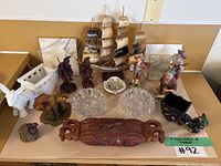 Full lot on table showing all figurines, crystal ashtrays, carved wood item, model ship, and other small decorative pieces.