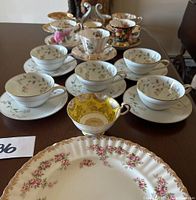 Group photo of all teacups and saucers along with a decorative plate, showing delicate floral patterns and gold trim on white fine china.