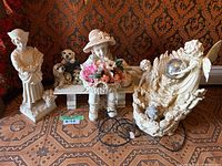 Three garden sculptures displayed together, showing the children and dog figurine and two angel sculptures all on tiled floor.