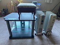 Two oil heaters and a TV stand with a small stool on top, arranged indoors near a window.
