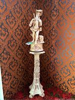 Full view of large figurine on tall decorative pedestal against patterned wallpaper.